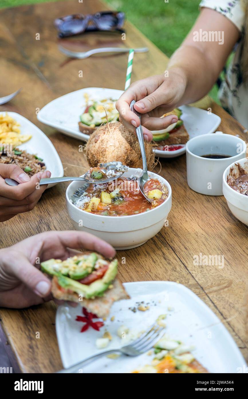 Gli amici potranno gustare una colazione vegetariana con pane tostato, uova strapazzate, cocco e avocado. Godendo la compagnia di amici e cibo. Atmosfera estiva Foto Stock