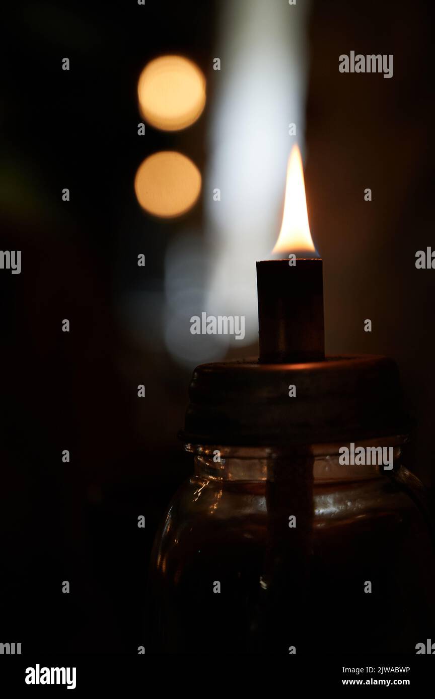 Fiamma singola su piccola lampada ad olio con sfondo scuro e sfocato Foto Stock