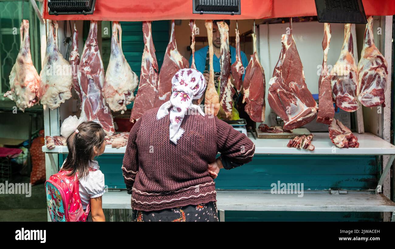 OSH, Kirghizistan - Maggio 2022: Donna non identificata esamina una varietà di carne all'aperto in una macelleria al mercato locale Foto Stock