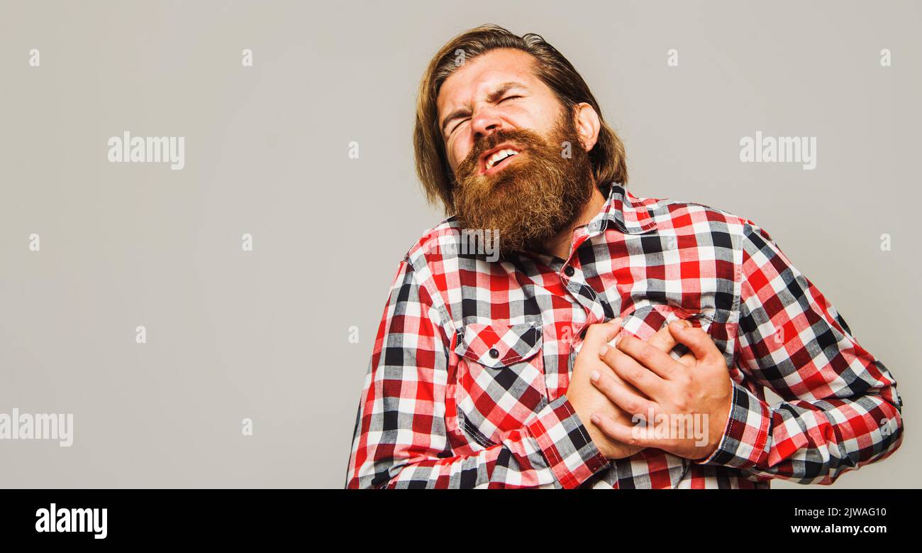 Uomo barbuto con dolore al cuore che tiene la mano sul petto. Infarto o ictus. Concetto di assistenza sanitaria. Foto Stock