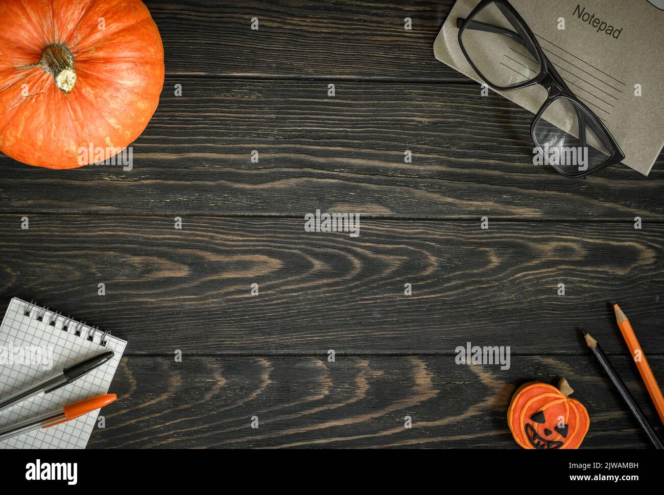 Sfondo di Halloween, vista dall'alto. Zucca e forniture scolastiche su tavolo di legno scuro, piatto. Cornice di Halloween arancio cibo, bicchieri e blocco note su woo Foto Stock
