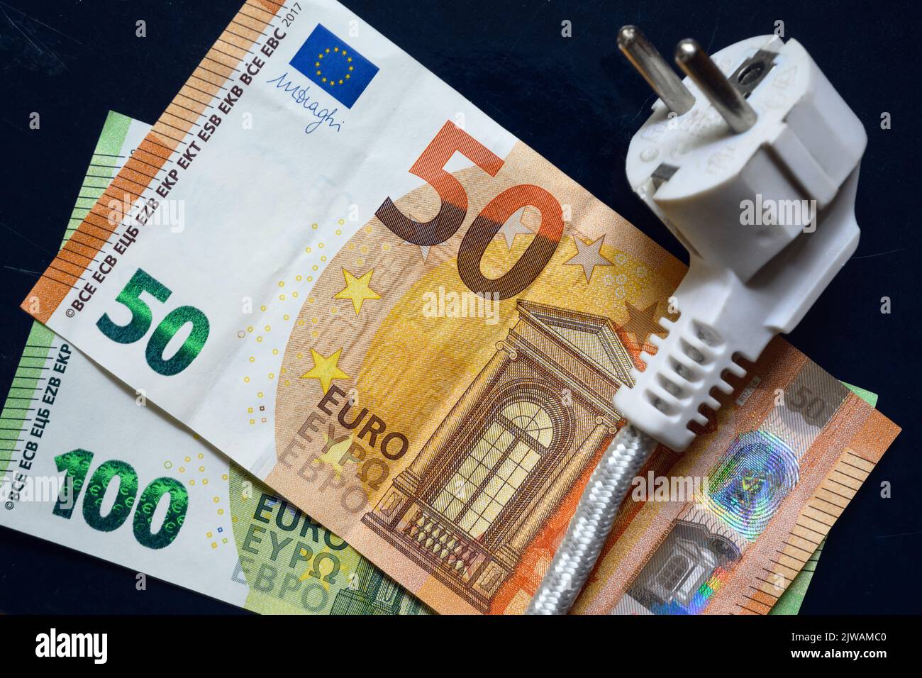 Spina di alimentazione e moneta in euro, cavo elettrico nazionale sulle banconote europee, vista dall'alto. Crisi energetica in Europa, prezzo dell'elettricità a casa costoso. Concetto Foto Stock