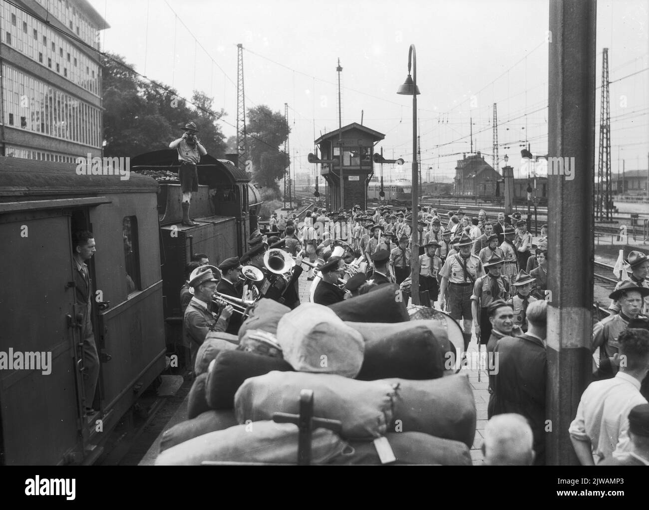 Immagine della partenza di un gruppo di scout in treno per il Jamboree in Austria sulla piattaforma della stazione N.S. Utrecht et al. A Utrecht, con un'orchestra d'armonia in primo piano, una locomotiva a vapore della serie 3700/3800 del N.S. E sullo sfondo il Seinhuis Post C. Foto Stock