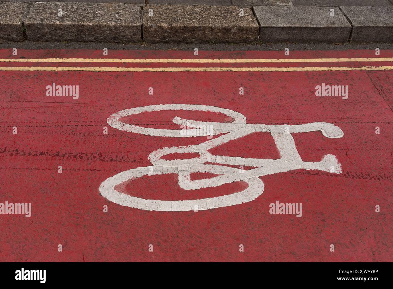 Plymouth, Devon, Inghilterra, Regno Unito. 2022. Bicicletta dipinta di bianco sul fondo stradale di colore rosso lungo una strada cittadina che mostra un marciapiede a discesa e una doppia linea gialla Foto Stock