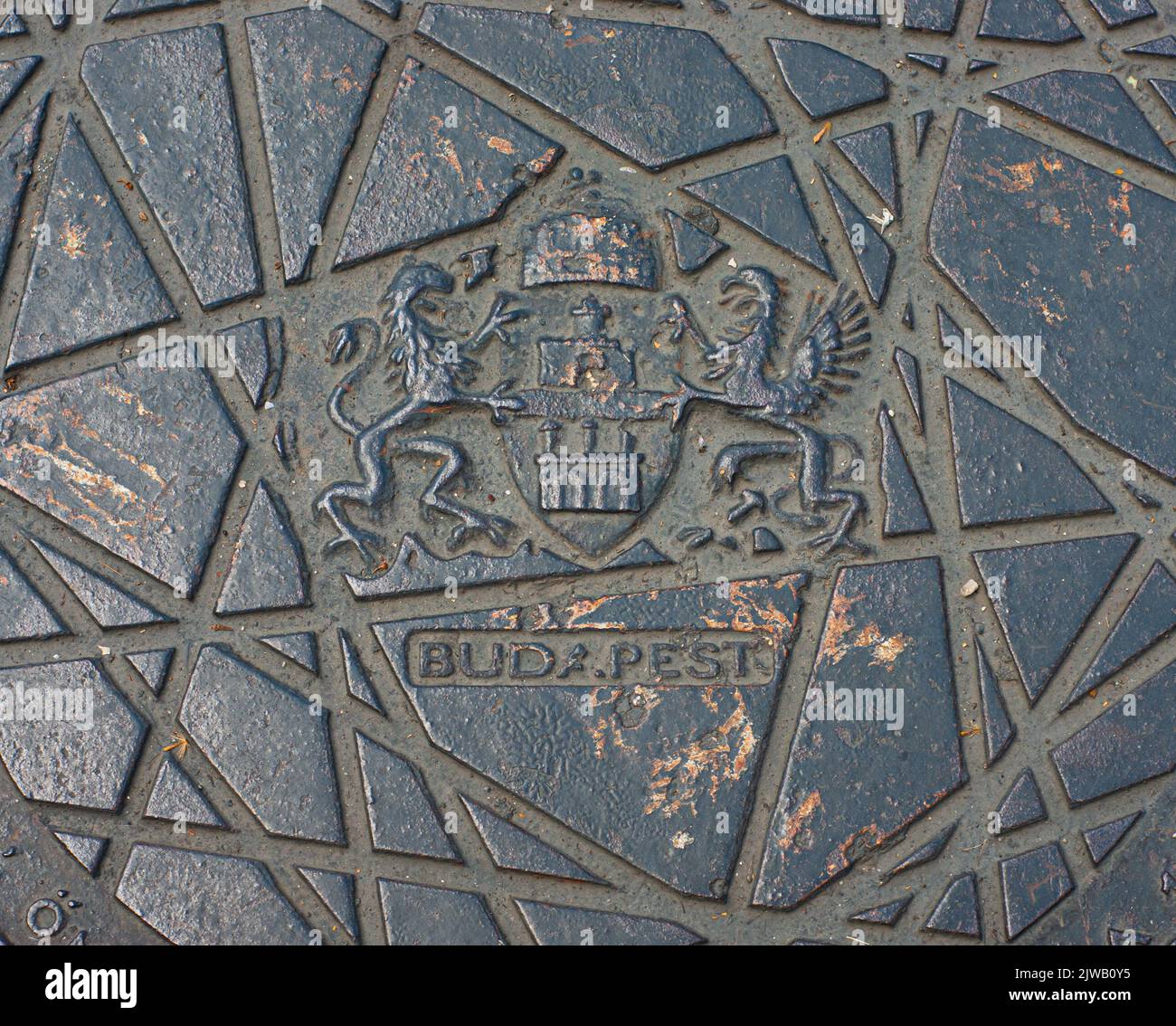 Ammira il primo piano di una botola fognaria sulla strada di Budapest, Ungheria. BUDA.PEST ha un periodo per mostrare due città. Vedere il simbolo dello stemma. Foto Stock