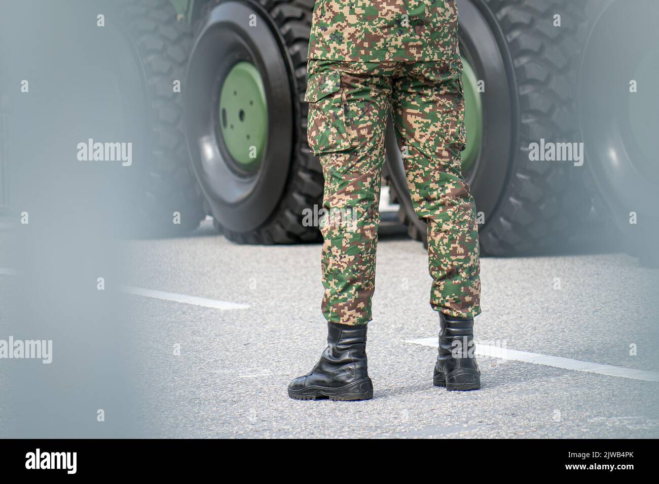 Primo piano delle gambe del soldato con stivali militari e pantaloni como, in piedi di fronte alla canotta metallica. Foto Stock