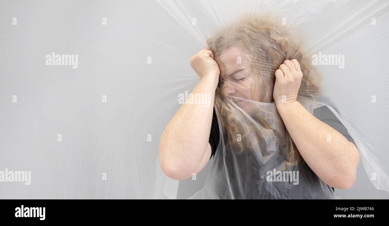 immagine concettuale sfocata ritratto arte di una donna matura afferrare la testa mal di testa, la posizione dietro pellicola di plastica trasparente pellicola, rappresenta il Foto Stock