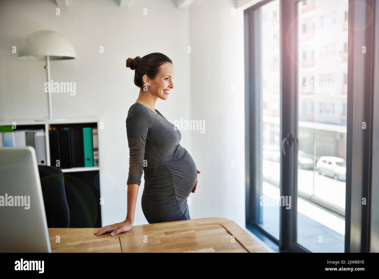 Youre quasi qui... una donna d'affari incinta in piedi nel suo ufficio che tiene il suo stomaco. Foto Stock