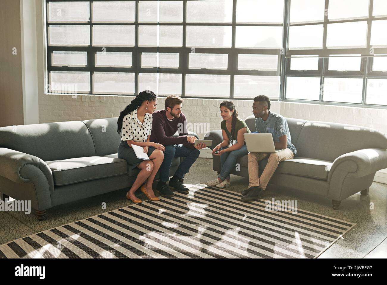 Contribuire al successo dell'azienda come team. Un team di colleghi che si riunisce su un divano in un ufficio moderno. Foto Stock