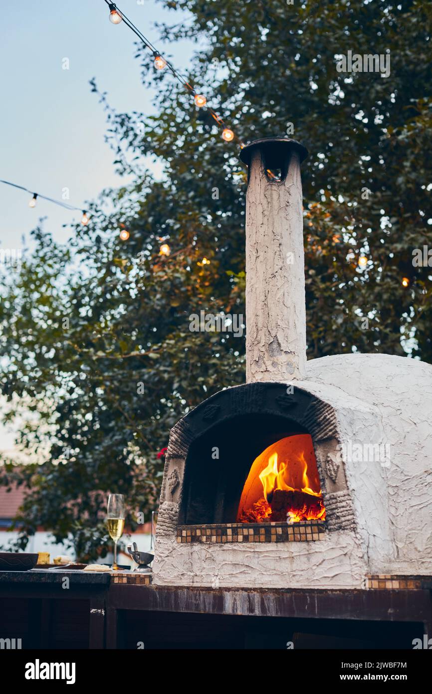 Forno a legna per pizza con tronchi di betulla per l'accensione. Il fuoco brucia e il forno si riscalda. Foto verticale. Foto Stock
