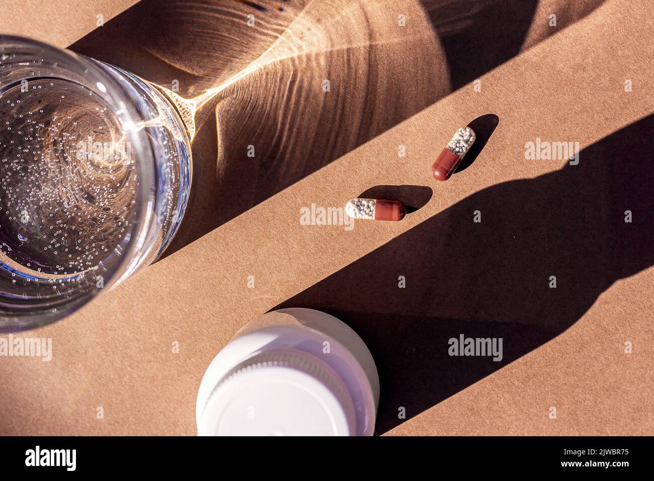 Pillole e bicchiere d'acqua su sfondo marrone. Medicina, concetto di assistenza sanitaria. Foto Stock