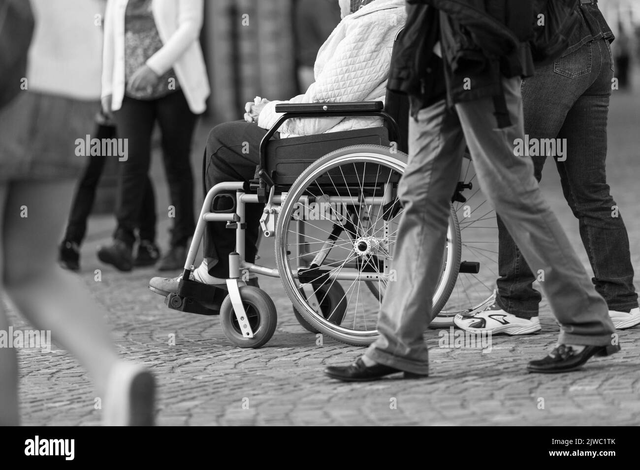Primo piano di una donna su una sedia a rotelle con un assistente durante la passeggiata nella strada trafficata. Foto Stock