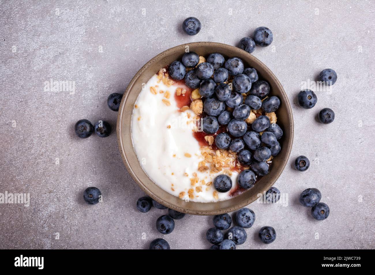 Vista dall'alto con ciotola di dessert sano o colazione con yogurt, mirtilli e muesli su sfondo grigio cemento Foto Stock