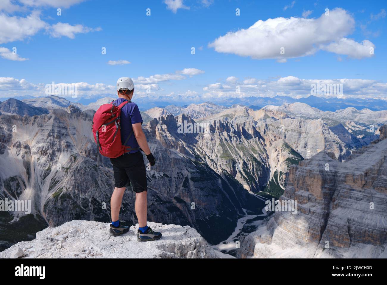Uomo escursionista con casco e zaino rosso ai margini di una scogliera sulle Dolomiti, Italia. Estate, attivo, attività, alpinismo, copia spac Foto Stock