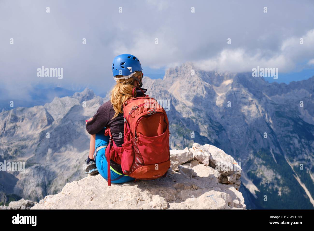 Una donna escursionista con zaino si siede sulla cima del Triglav e guarda le montagne circostanti nelle Alpi Giulie, Slovenia. Estate, attivo, attivo Foto Stock