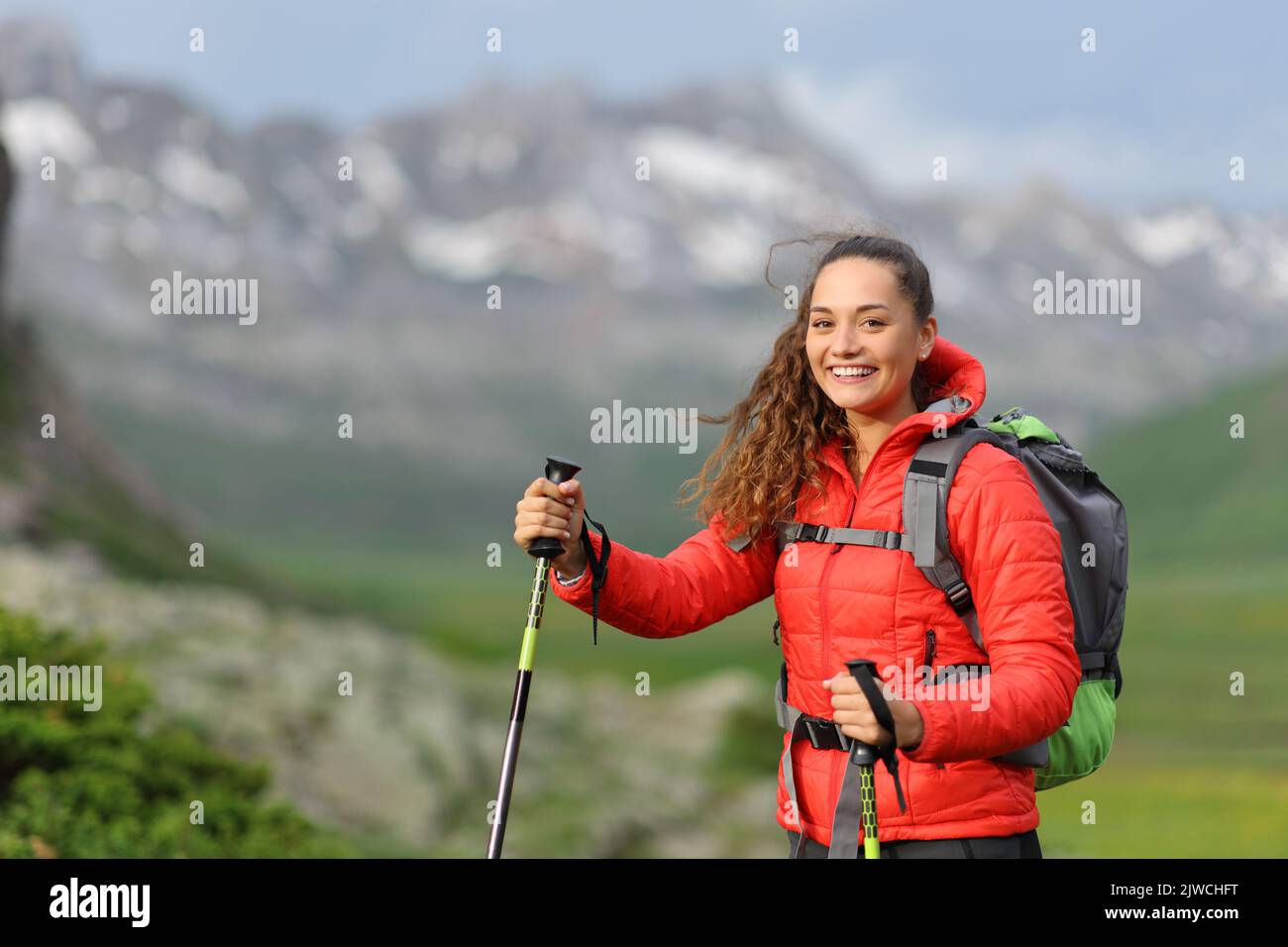 Buon escursionista in rosso guardando la macchina fotografica a piedi in montagna Foto Stock