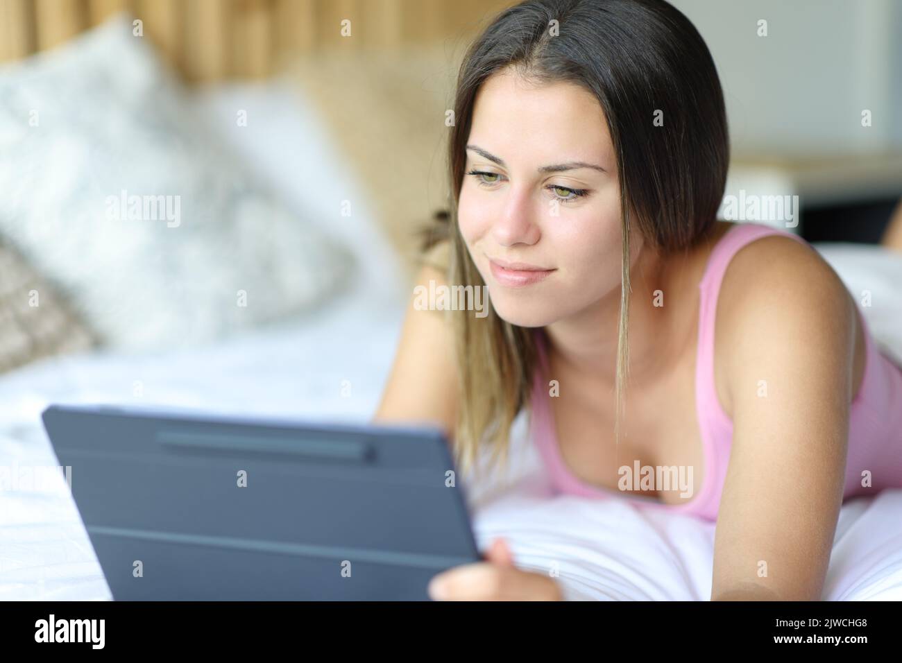 Donna felice che usa un tablet digitale sdraiato su un letto a casa Foto Stock