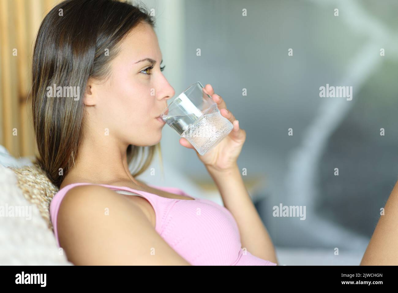 Vista laterale ritratto di una giovane donna che beve acqua su un letto a casa Foto Stock