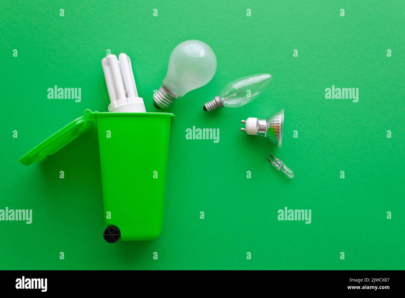 Concetto di stop allo spreco di energia: Vecchie lampadine alogene e fluorescenti diverse sulla loro strada in un contenitore di riciclaggio, sfondo verde, testo o spazio di copia. Foto Stock