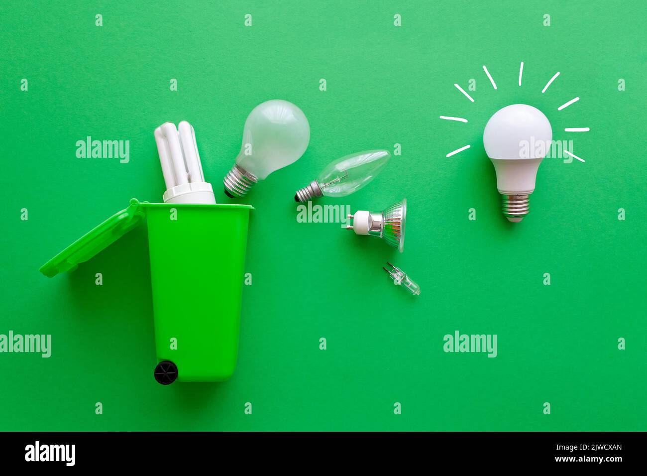Concetto di risparmio di elettricità: Nuova lampadina a LED a risparmio energetico brillante rispetto a diverse lampadine inefficienti vecchie in arrivo in un bidone di riciclaggio verde. Foto Stock