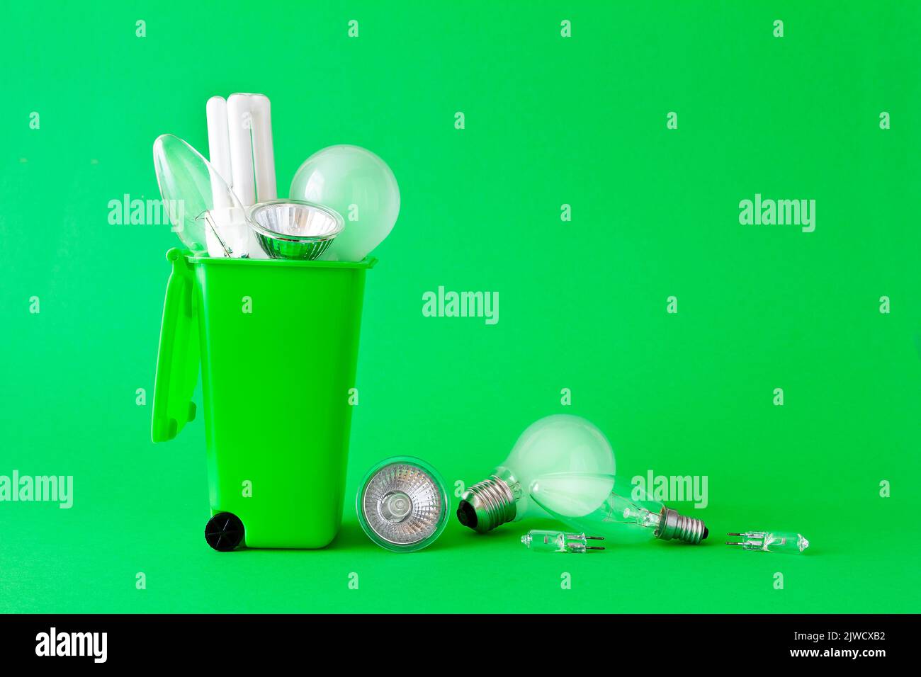 Concetto di Green Living: Diverse vecchie lampadine alogene e fluorescenti dentro e intorno a un contenitore di riciclaggio, sfondo verde, testo o spazio di copia. Foto Stock