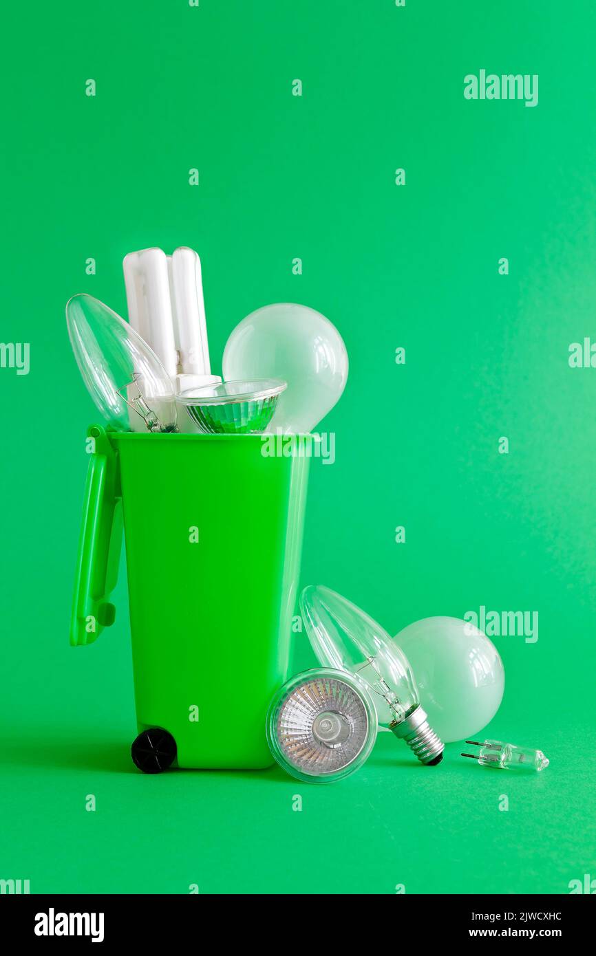 Concetto di risparmio di rifiuti di elettricità: Vecchie lampadine alogene e fluorescenti diverse all'interno e intorno a un contenitore di riciclaggio, sfondo verde, testo o spazio di copia. Foto Stock