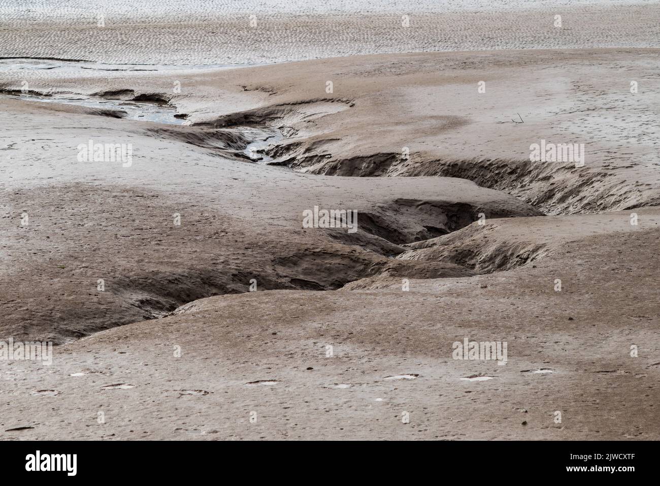 Canale dell'acqua che si snoda attraverso fango e sabbia veloce lasciato dalla bassa marea su mud flats Foto Stock