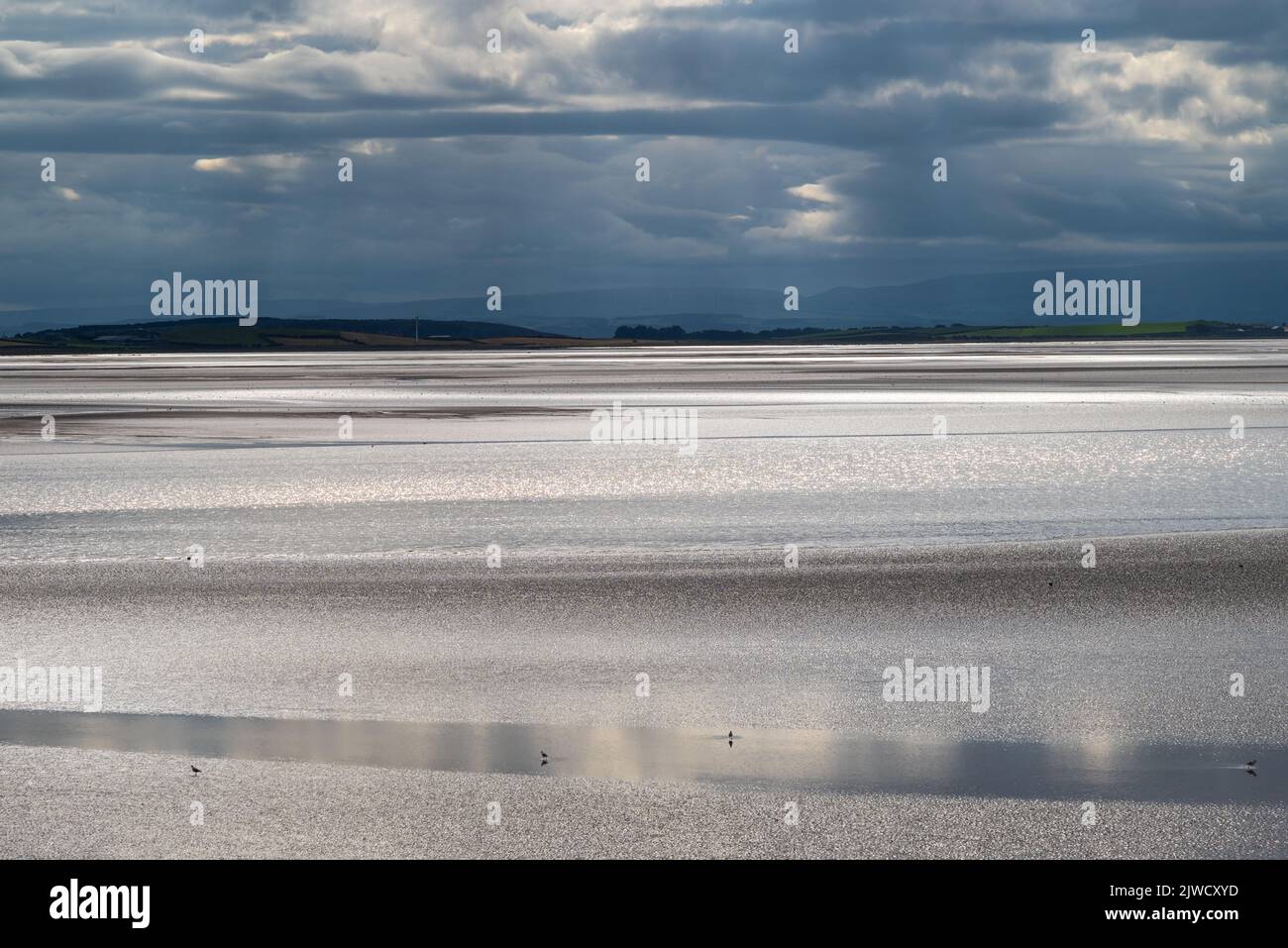 Paesaggio di Moody con nuvole scure, cielo scuro e luce solare che si riflette al largo del mare. Vista sulla baia di Morecambe da Canal Foot, Ulverston, Cumbria, Regno Unito Foto Stock
