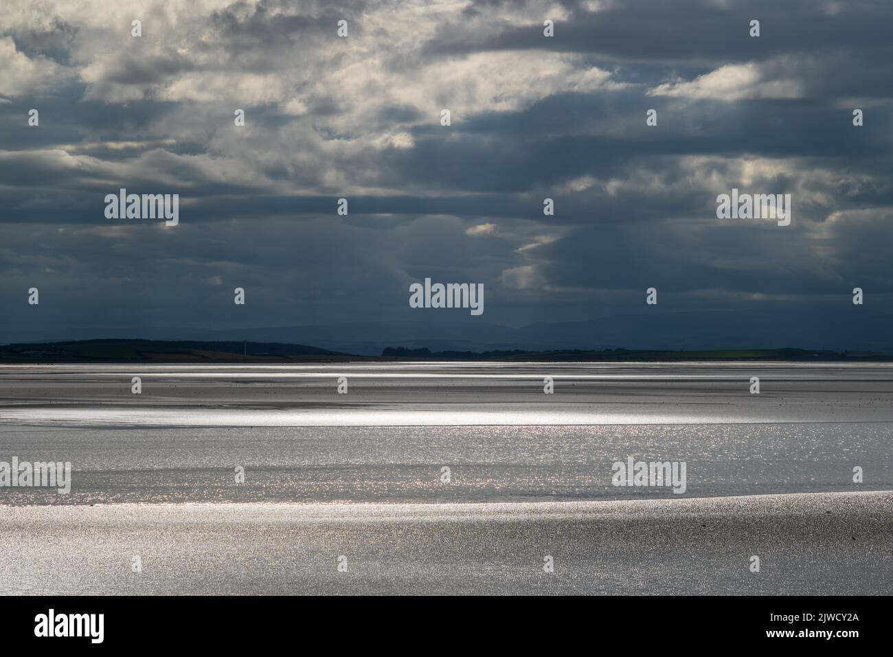 Paesaggio di Moody con nuvole scure, cielo scuro e luce solare che si riflette al largo del mare. Vista sulla baia di Morecambe da Canal Foot, Ulverston, Cumbria, Regno Unito Foto Stock