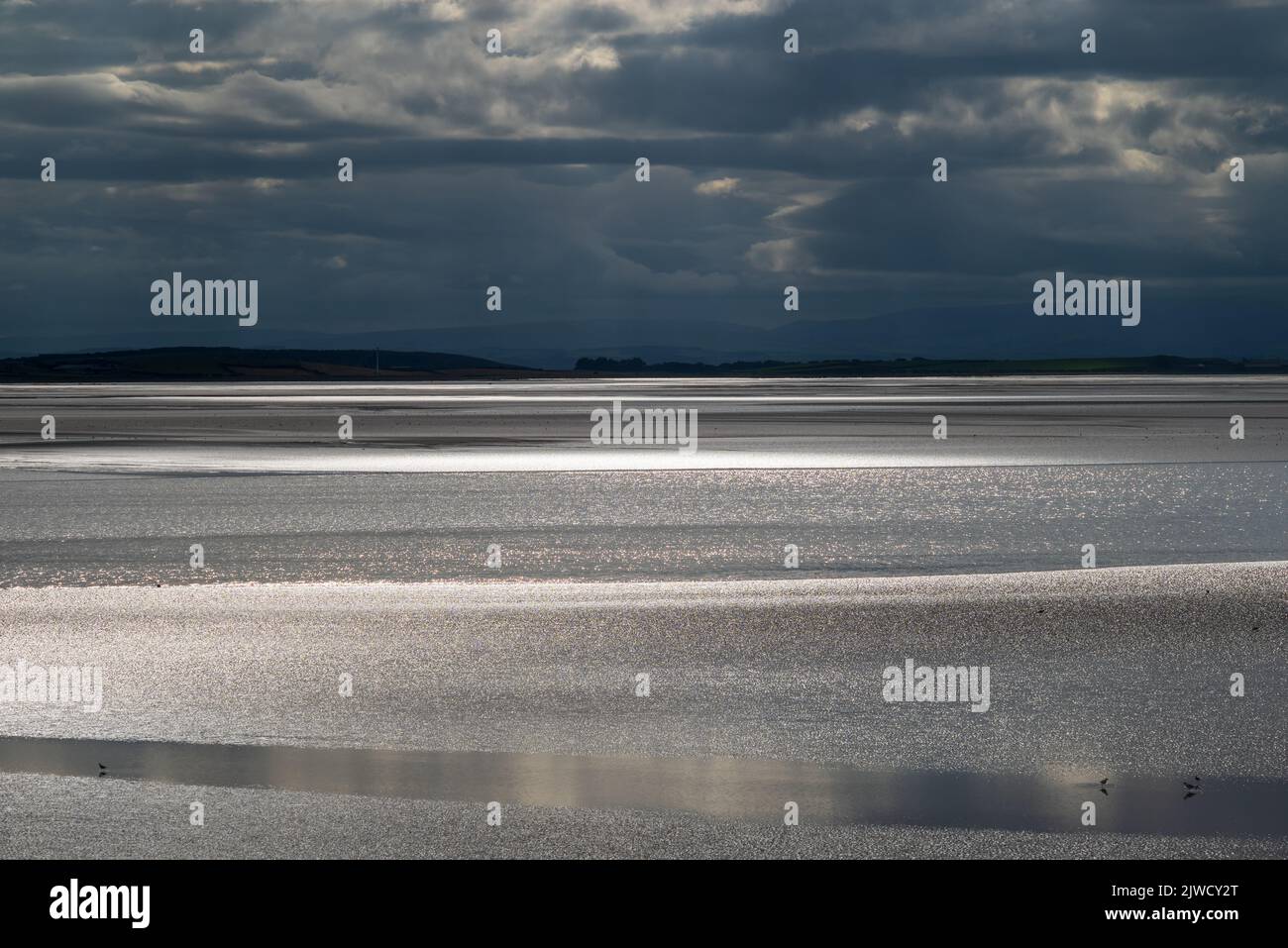 Paesaggio di Moody con nuvole scure, cielo scuro e luce solare che si riflette al largo del mare. Vista sulla baia di Morecambe da Canal Foot, Ulverston, Cumbria, Regno Unito Foto Stock