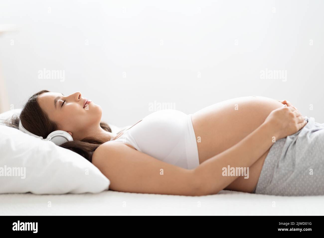Felice giovane donna incinta ascoltando la musica nelle cuffie Foto Stock