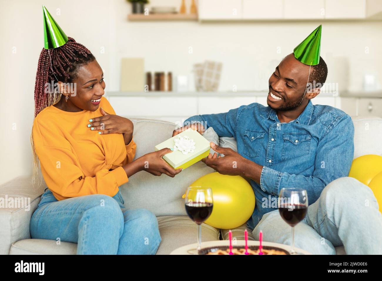 L'uomo nero amorevole saluta la moglie con il compleanno a casa, il marito  che dà la sua scatola regalo e sorridente, seduto insieme sul divano Foto  stock - Alamy