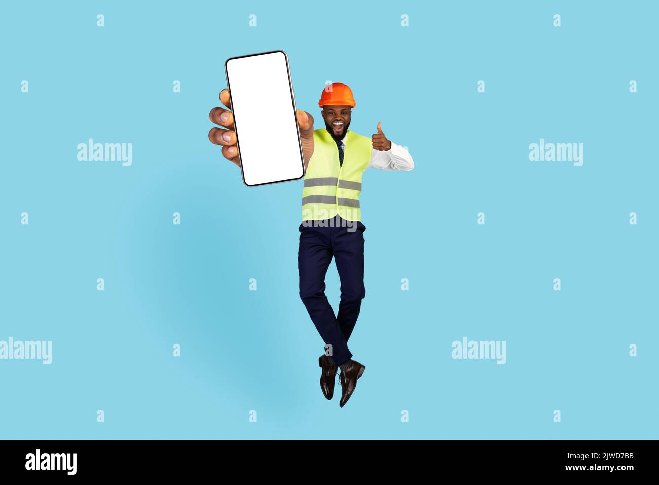 Ingegnere nero con smartphone vuoto in mano saltando e mostrando il pollice in alto Foto Stock