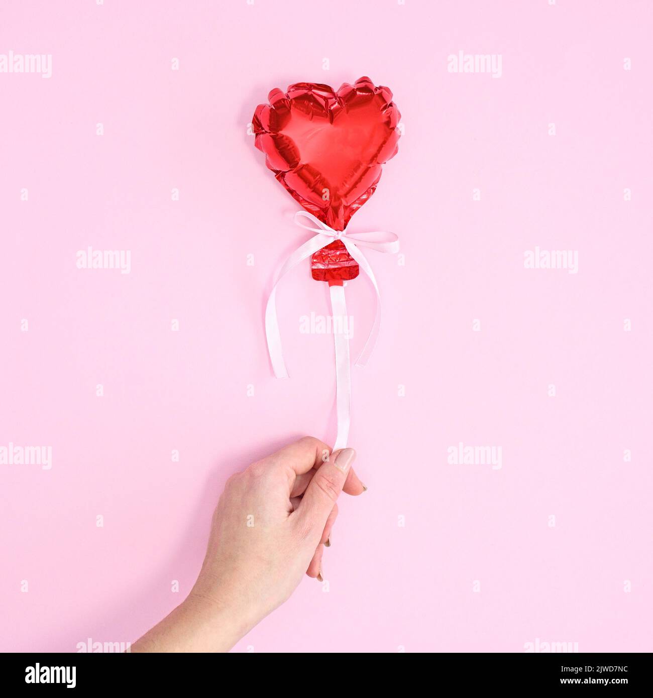 Donna che tiene palloncino cuore rosso per non volare via su sfondo rosa pastello. Piatto Lay San Valentino concetto giorno Foto Stock