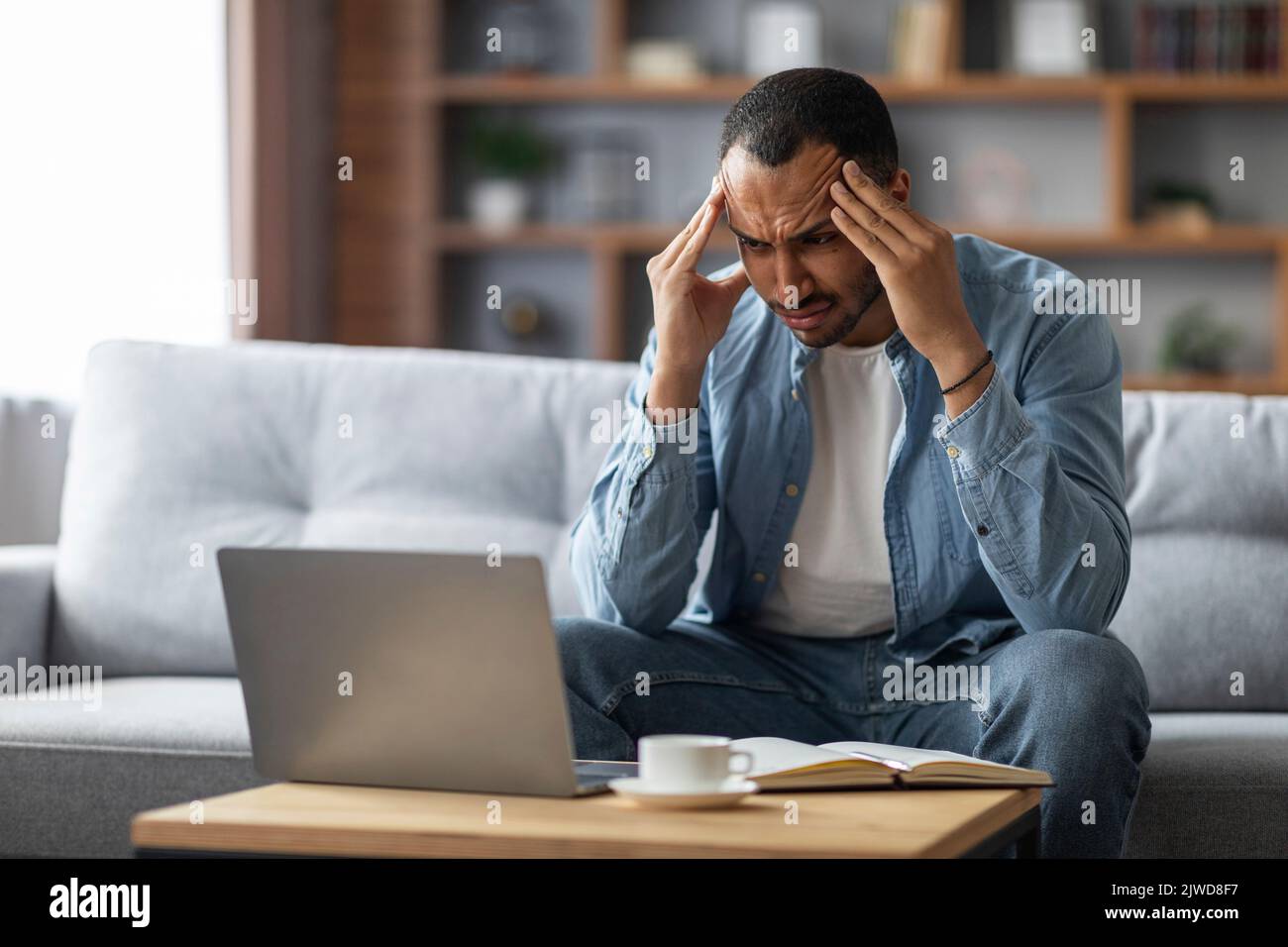 Stress freelance. Un ragazzo nero stanco che guarda lo schermo del notebook e i templi dello sfregamento Foto Stock