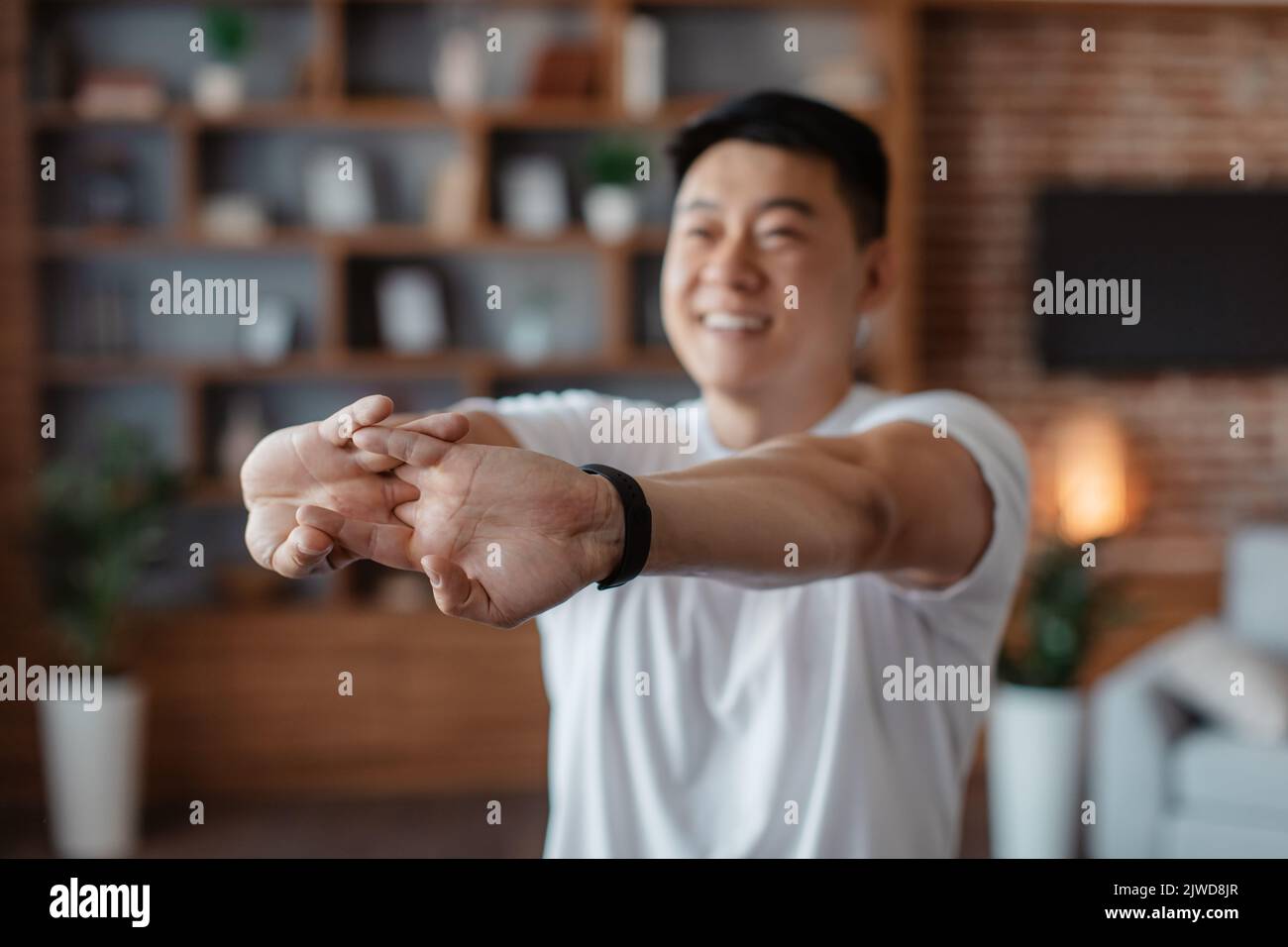 Uomo maturo coreano felice allungando le braccia prima di allenamento domestico, riscaldando le mani durante l'allenamento a casa Foto Stock
