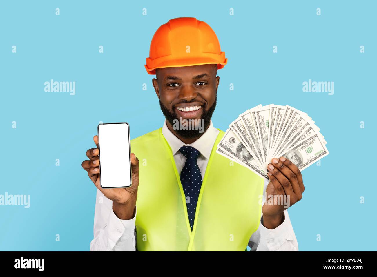 Allegro lavoratore della costruzione nera che tiene denaro contante e smartphone vuoto Foto Stock