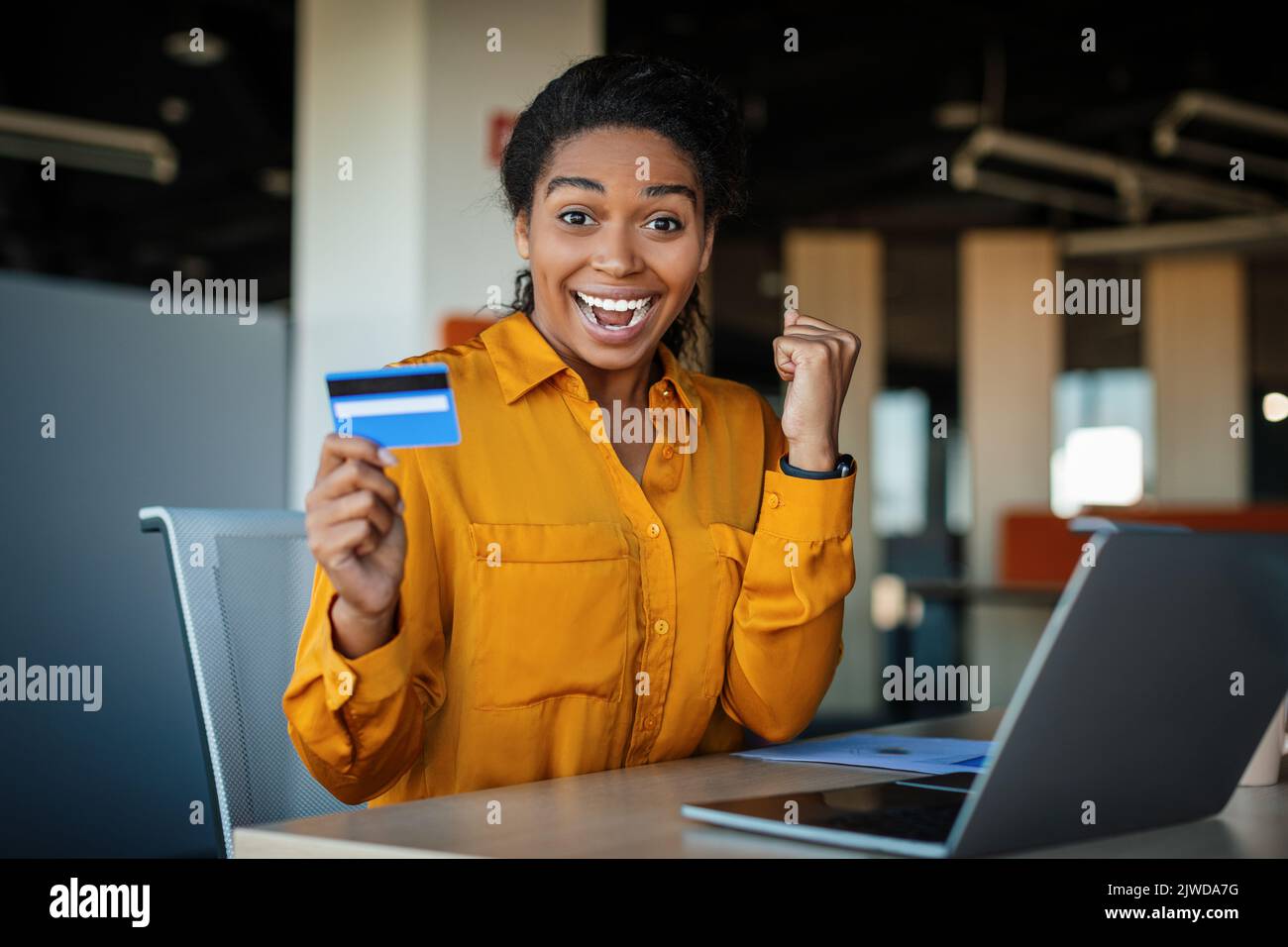 Overjoyed donna lavoro in ufficio con carta di credito, shopping in negozio on-line sul computer portatile, gesturing sì Foto Stock