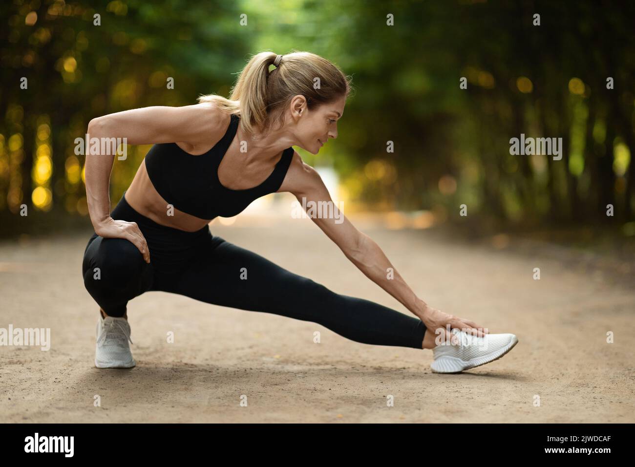 Donna attiva bionda di mezza età che si allunga nel parco pubblico Foto Stock