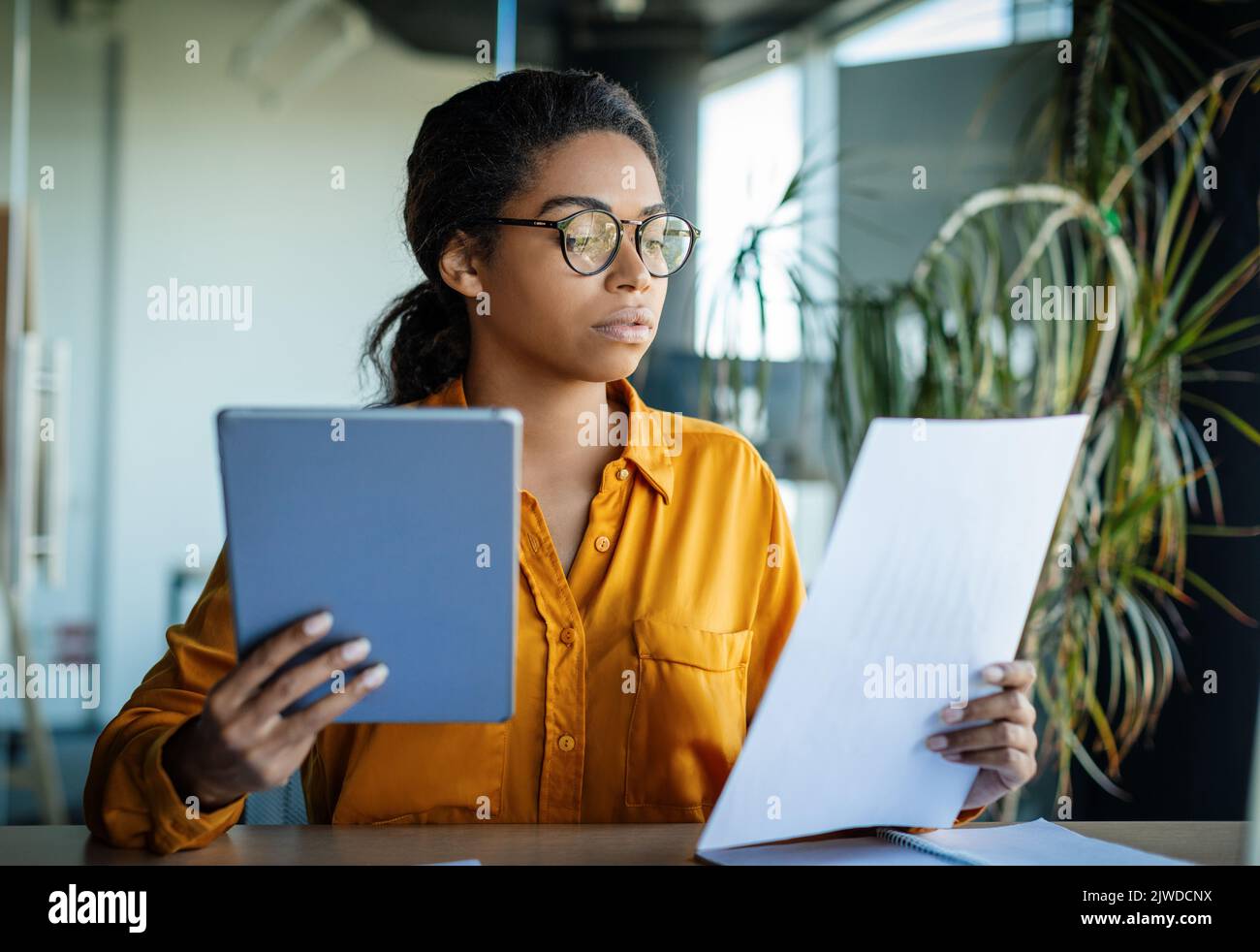 Seria imprenditrice nera che usa il tablet digitale e che legge i documenti, che lavora attraverso i documenti finanziari Foto Stock