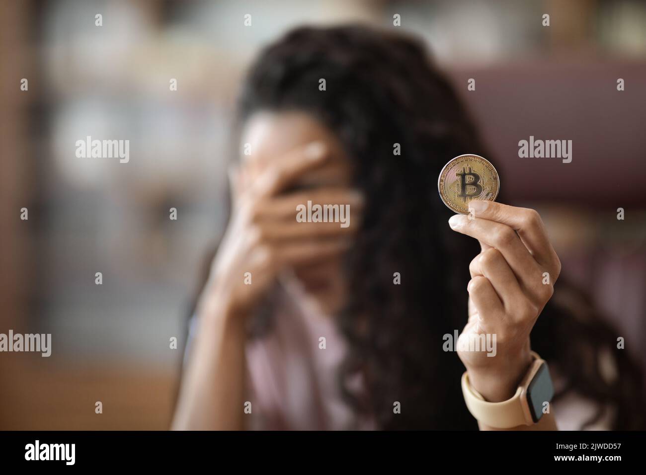 Giovane donna in possesso di moneta virtuale bitcoin in ufficio Foto Stock