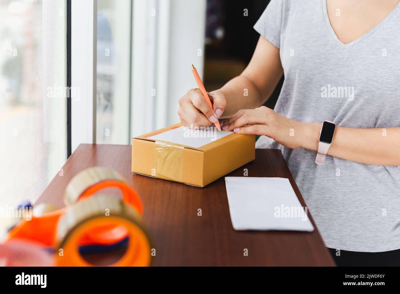 Donna che scrive l'indirizzo sulla scatola di cartone nell'ufficio postale Foto Stock