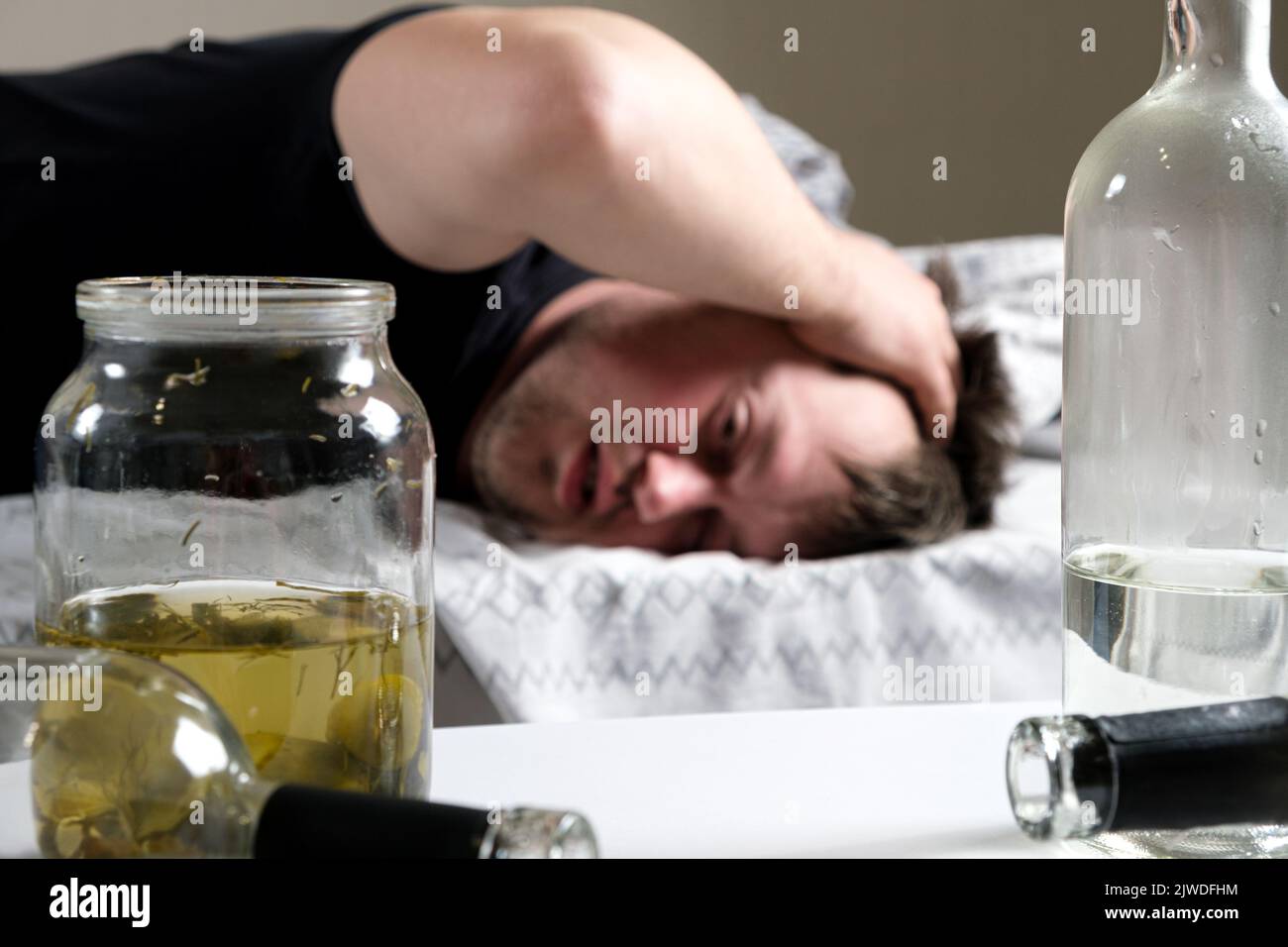 Un uomo ubriaco si trova a letto, tenendogli le mani in testa. Hangover, delirio alcolico. Foto Stock