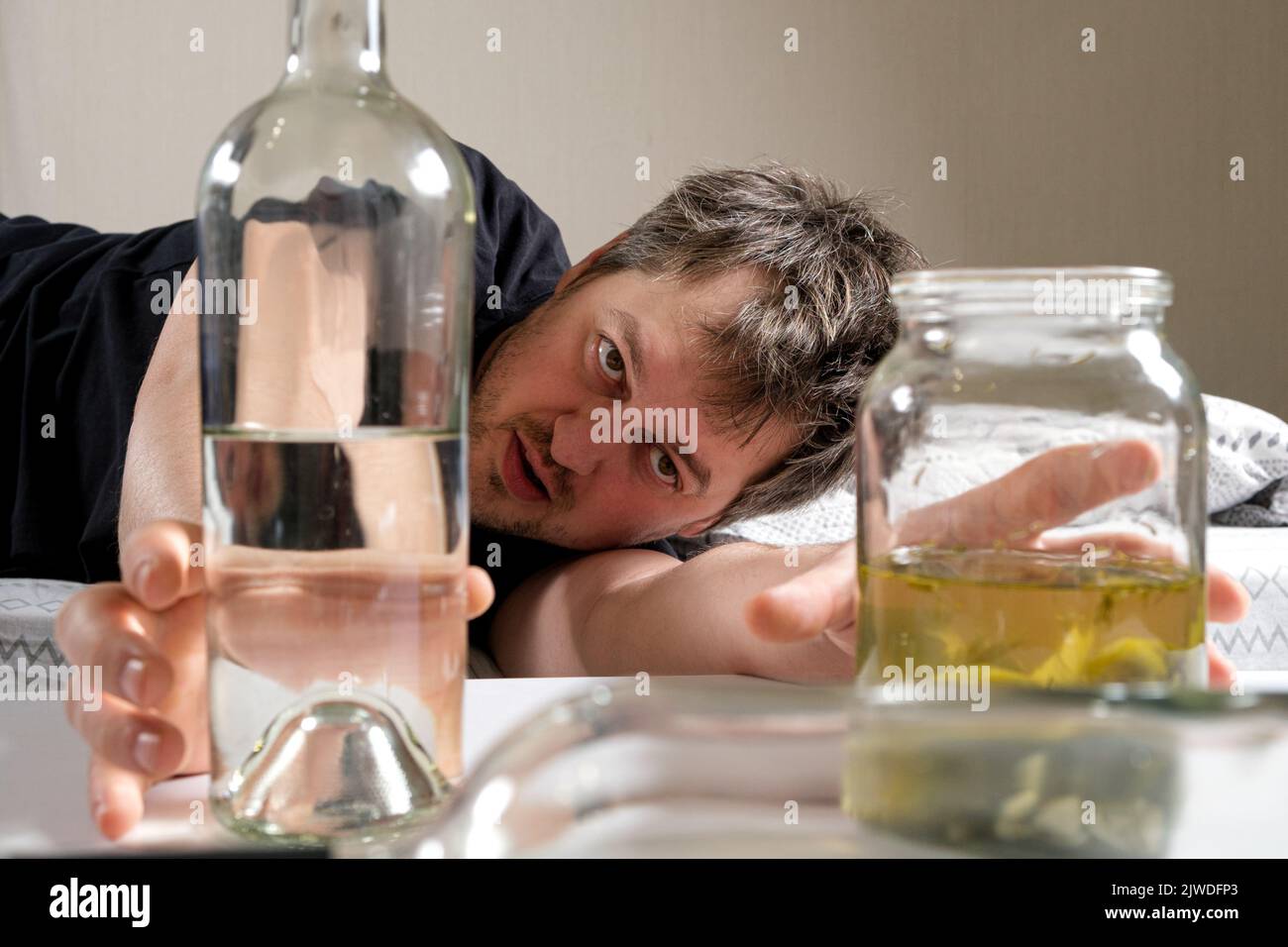 Un uomo ubriaco con dipendenza da alcol prende una bottiglia di vodka e salamoia con sottaceti sottaceto. Foto Stock
