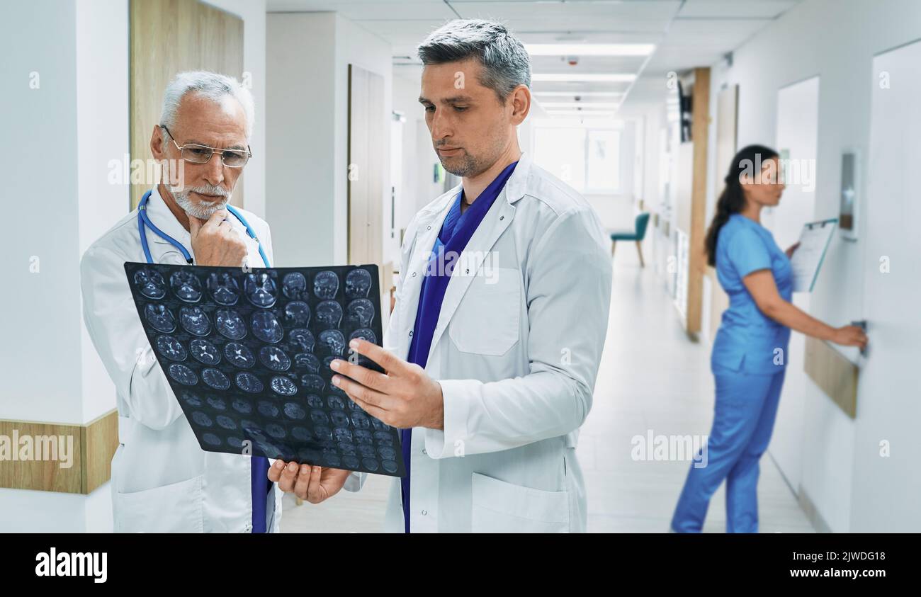 Due medici che analizzano la risonanza magnetica del cervello del paziente mentre si trovano nel corridoio della clinica moderna durante la giornata lavorativa. lavoro di squadra medico Foto Stock