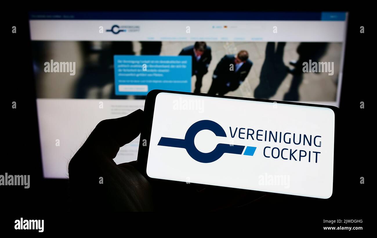 Persona che tiene il cellulare con il logo dell'associazione pilota tedesca Vereinigung Cockpit sullo schermo di fronte alla pagina web. Messa a fuoco sul display del telefono. Foto Stock