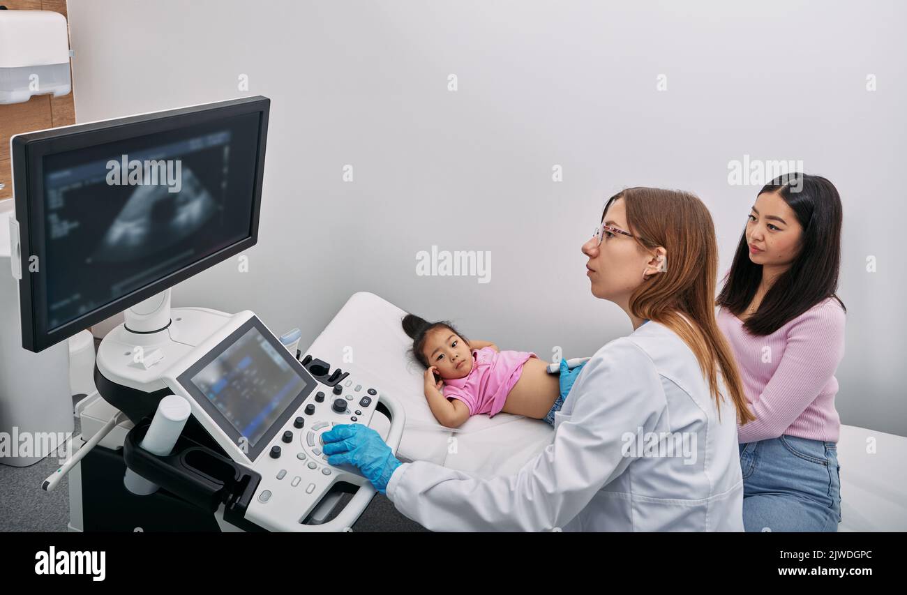Bambina coreana con il sostegno di sua madre, che ha procedura ecografica di organi interni con ecografista in clinica medica. Addominale pediatrico Foto Stock