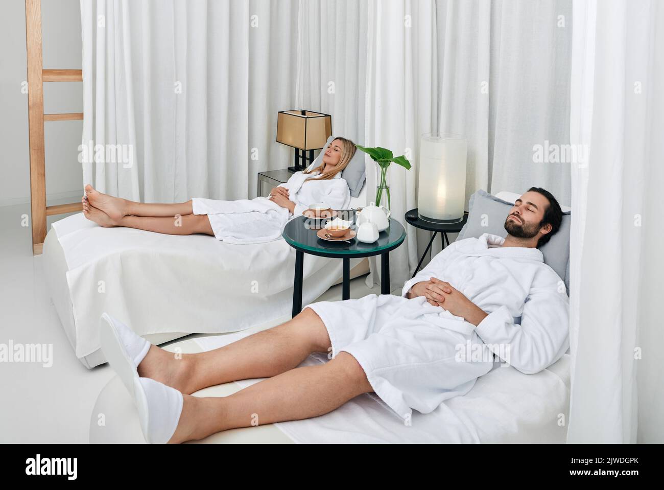 Rilassante bella coppia con gli occhi chiusi adagiarsi su letti bianchi, riposarsi nella zona lounge del centro benessere dopo le procedure spa Foto Stock