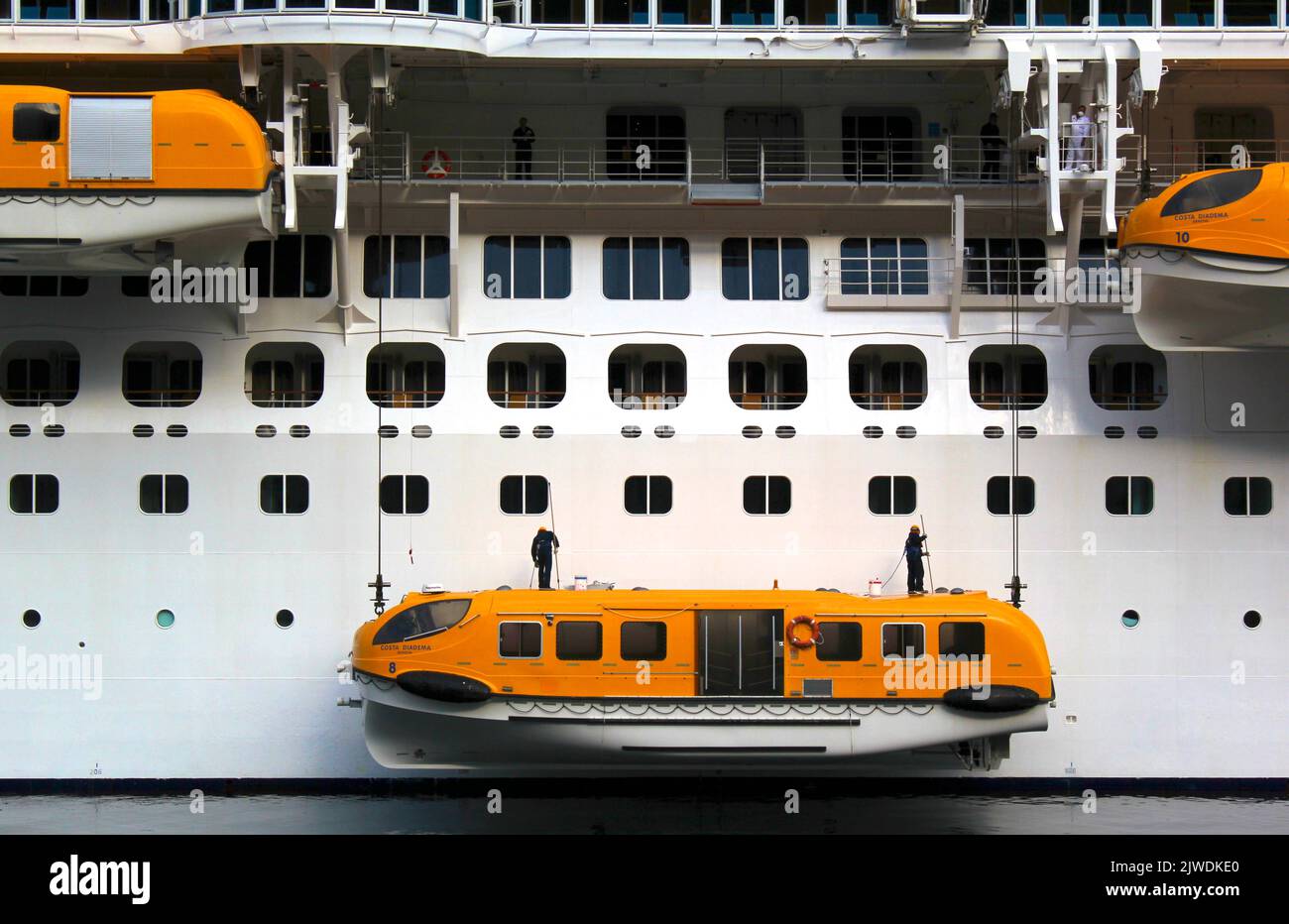 Enorme nave da crociera che viene ripulita da uomini che equilibrano su navi di salvataggio che sono sospesi sul lato Foto Stock