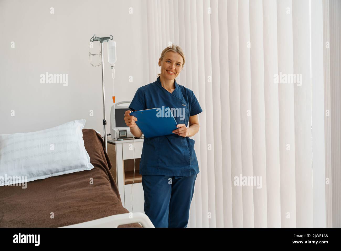 Un'infermiera sorridente che tiene un tablet mentre è in piedi nel reparto ospedaliero pronto a lavorare Foto Stock